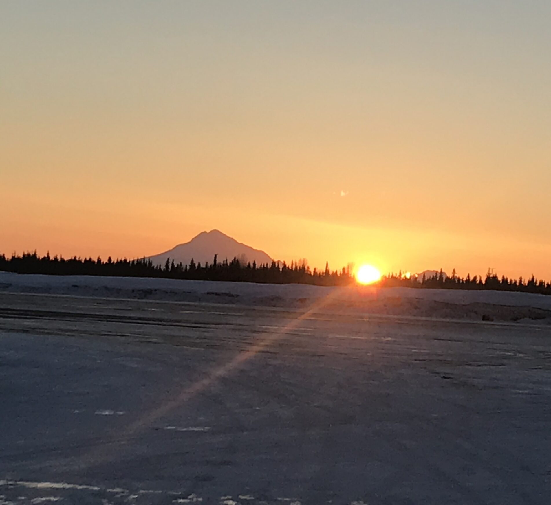 View from Kenai airport - sun setting next to Mt. Reboubt. Sunbeams coming over the runway.